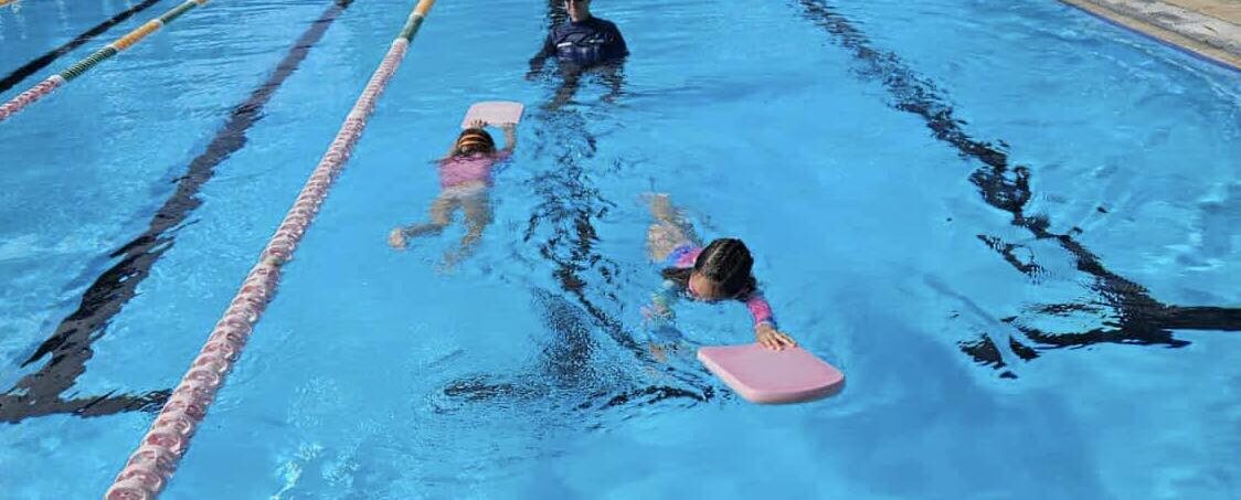 Featured is an image of two children having a swimming lesson with an instructor in the pool at Tilligerry Aquatic Centre.