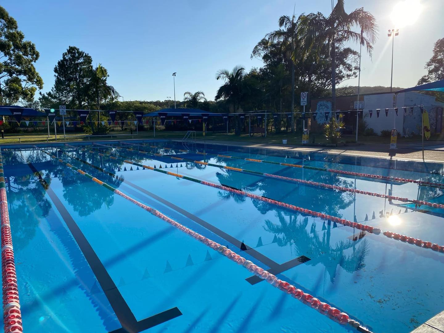 Features the 25m outdoor heated pool at Tilligerry Aquatic Centre during the afternoon. The blue water in the pool appears still. Nobody is in the pool.